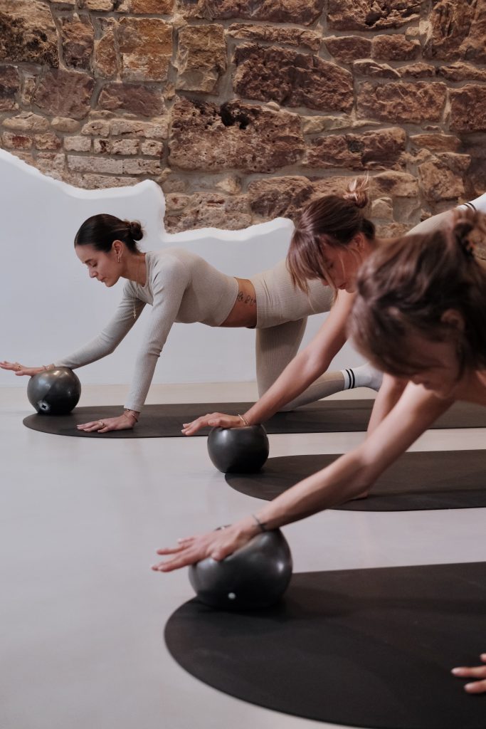 Drei Schülerinnen mit Ball unter der rechten Hand in einer Pilates Matten Klasse